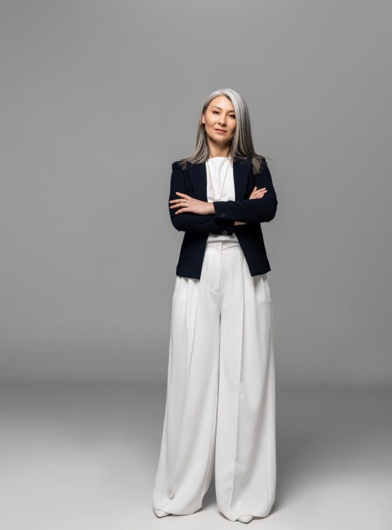 confident asian businesswoman with grey hair and crossed arms on grey